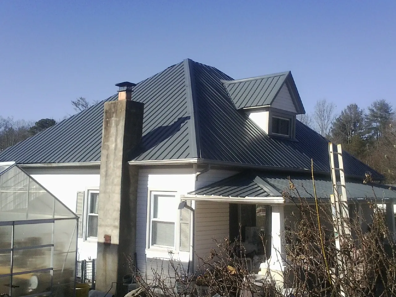 Dark blue standing seam metal roof on a white farmhouse with dormer — Slate & Tile Roof Repair by Roofing Brothers in Dannemora