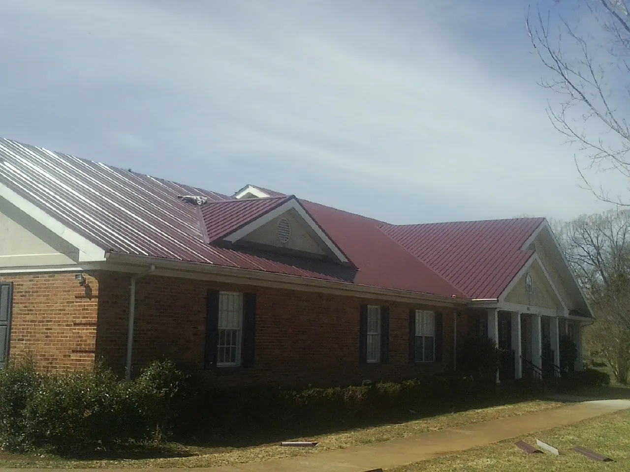 Red metal roof with gabled entries on a long brick building, from a Hail Damage Roof Repair job in Dannemora