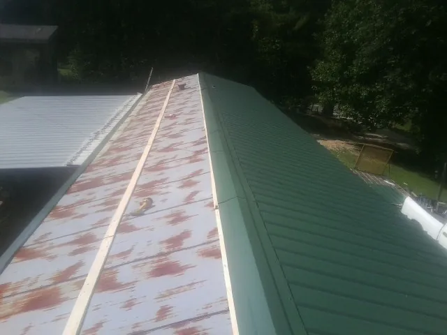 Old rusted panels beside newly installed green metal roofing — Wind Damage Roof Repair by Roofing Brothers in Dannemora