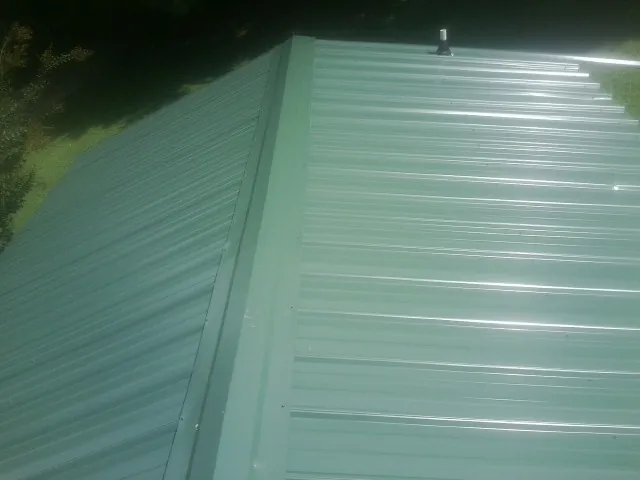 New green metal panels meeting at the ridge of a roof — Flat Roof Repair work by our crew in Dannemora