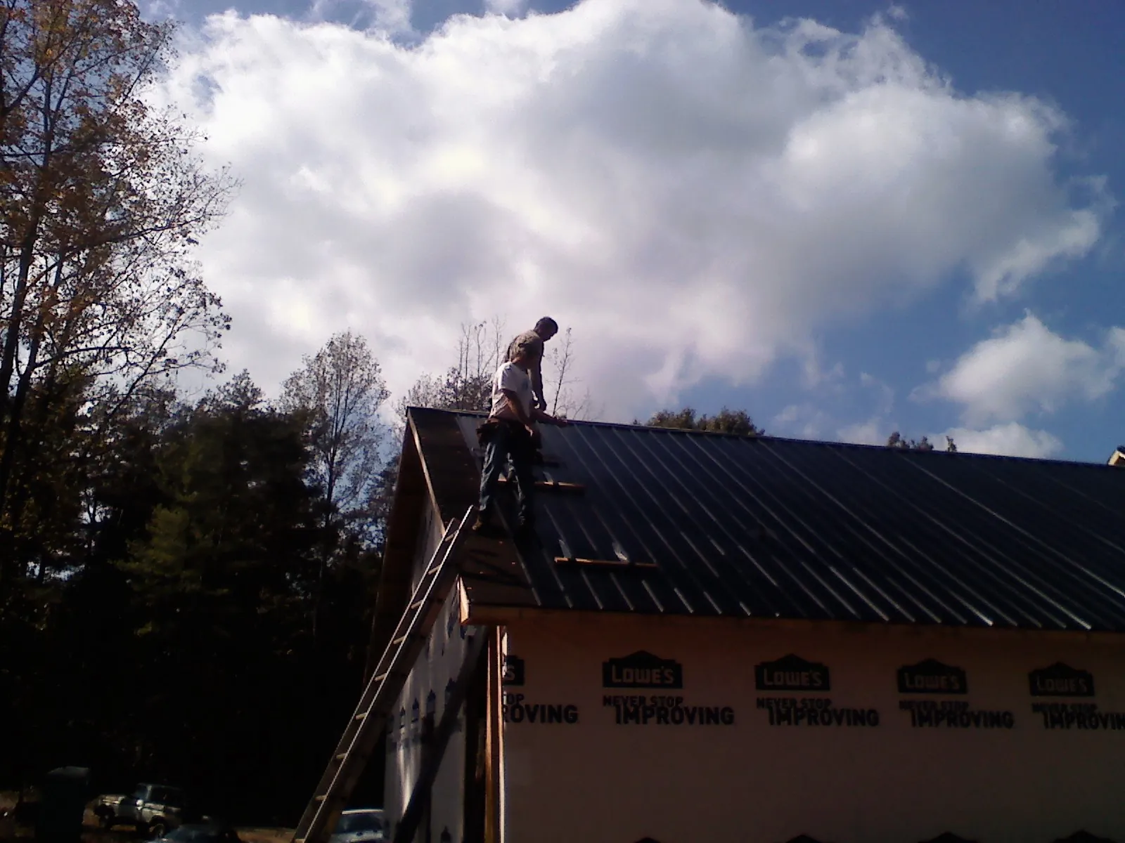Roofer fastening dark metal panels high against a cloudy sky, from a Roof Inspection job in Dannemora