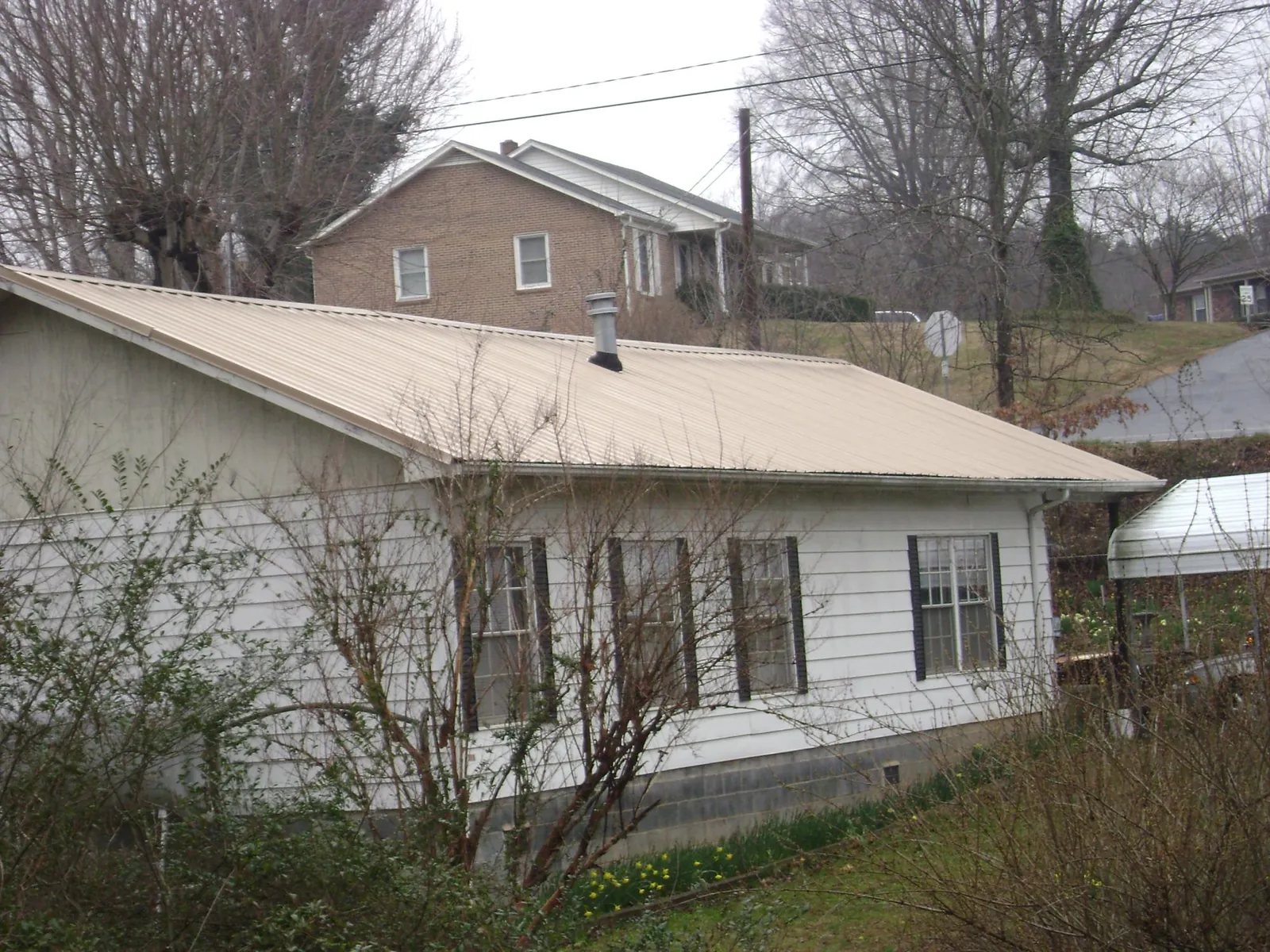 Tan metal roof on a white sided house set into a hillside — Commercial Roofing by Roofing Brothers in Dannemora