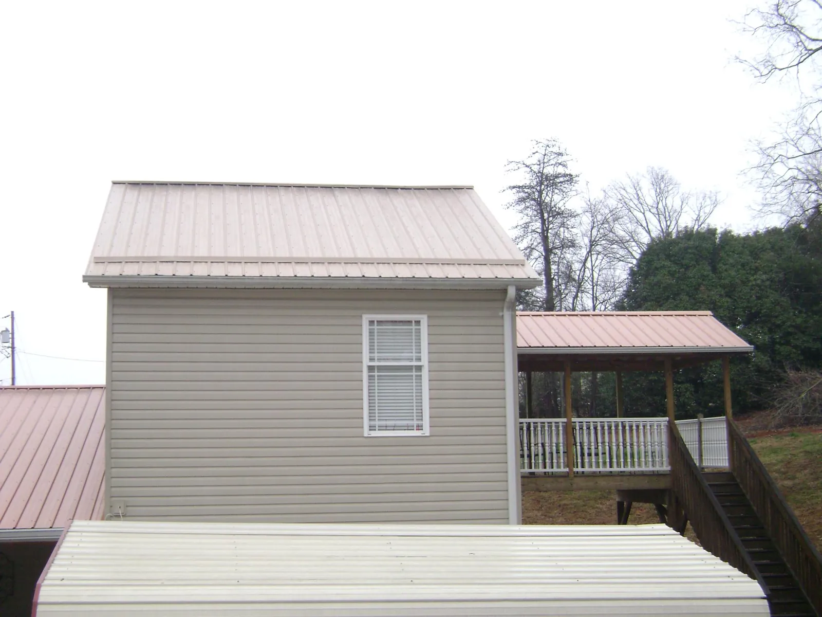 Tan metal roofs on a two story addition and attached porch, from a Roof Replacement job in Dannemora